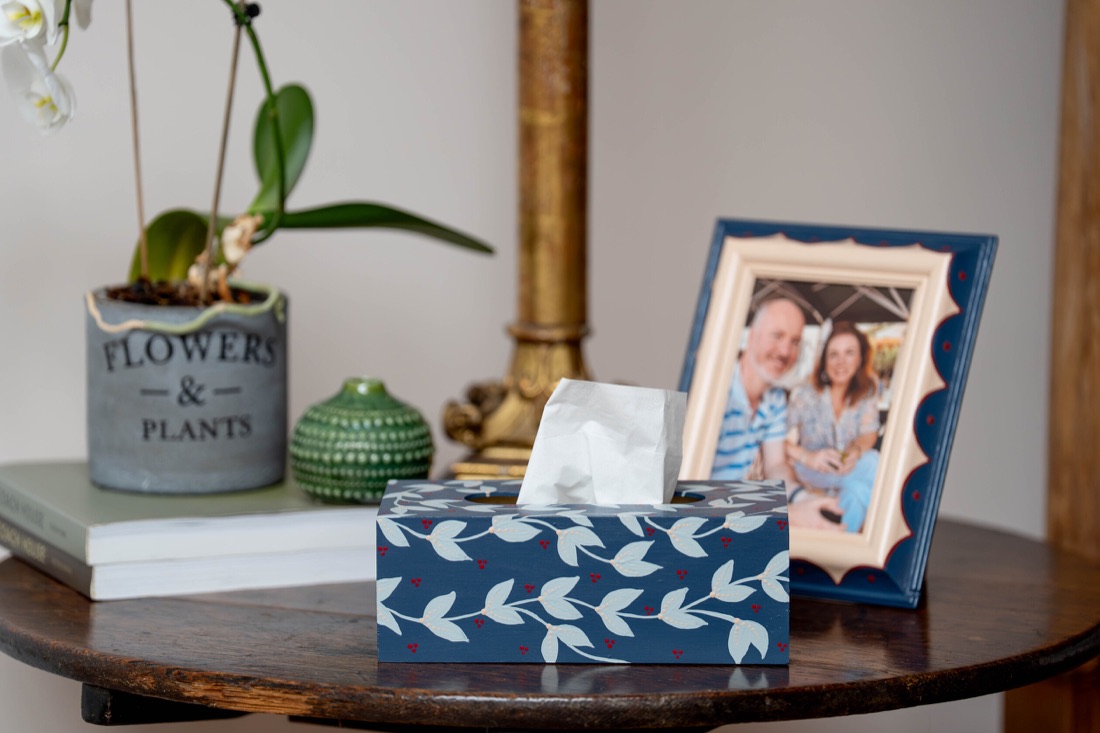 A navy tissue box painted with white leaves beside a blue picture frame.