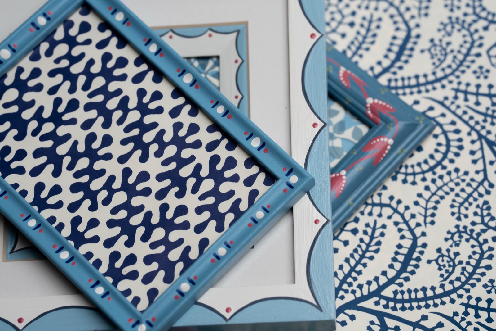 Blue hand-painted frames with scalloped and dotted details, arranged over blue and white patterned paper.