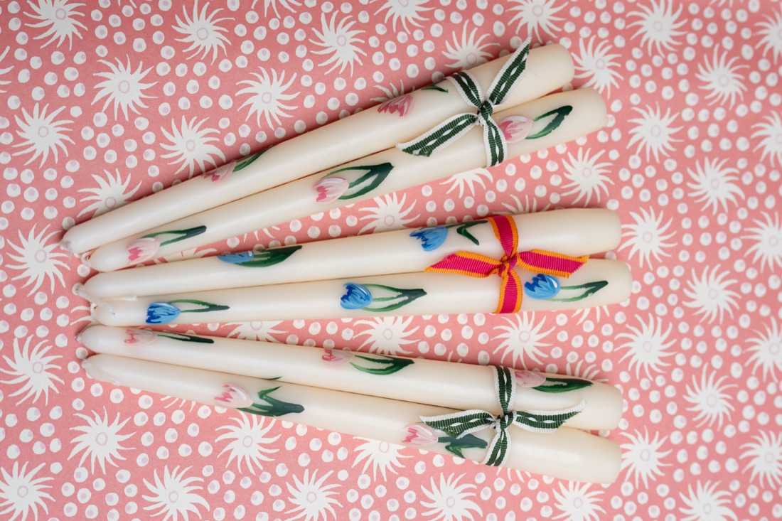 Hand-painted floral candles, tied in pairs with colourful ribbons.