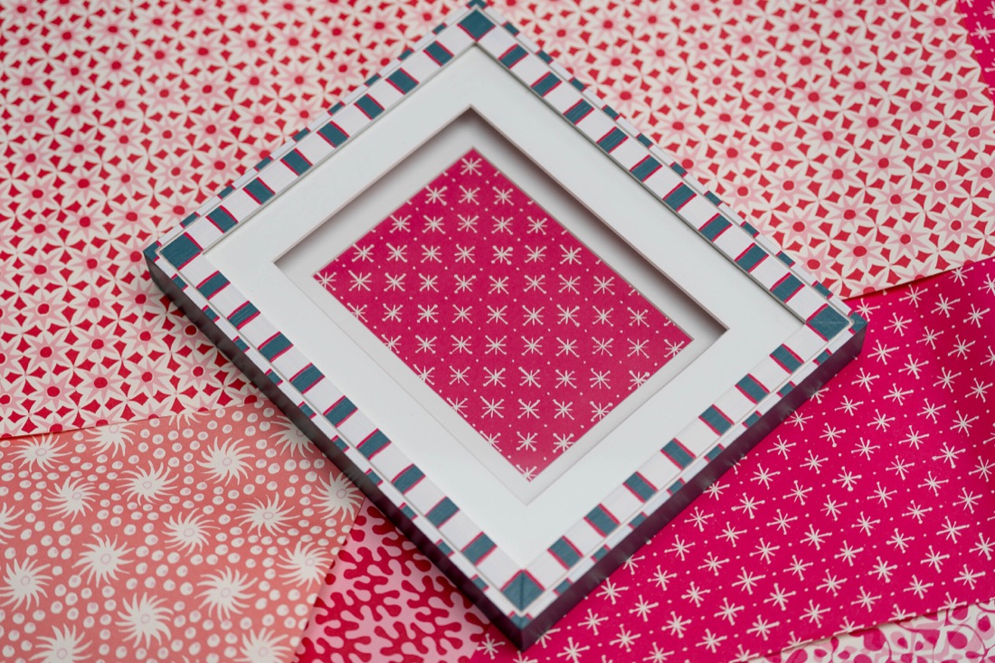 A white picture frame with blush and navy checks along its edge.